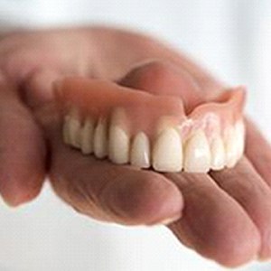 A person holding a custom-made full denture designed to replace missing teeth along the top arch