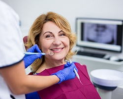 An older woman smiling at her dentist while they check her teeth and implants for any possible damage during a checkup