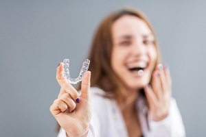 Laughing woman blurry in background holding Invisalign to foreground