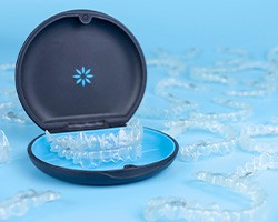 Several Invisalign trays surrounding carrying case with blue background