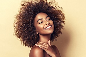 A young woman with her eyes closed and smiling to show off her new and improved smile