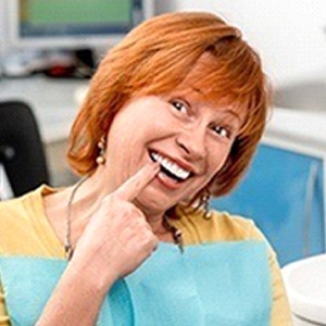 A middle-aged woman with red hair points to her new dentures during a dentist’s appointment