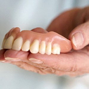 A person holding a full denture designed for the top arch of the mouth