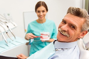 An older man smiling after receiving his dentures in Carrollton while a dental hygienist shows him how to keep his prosthetics clean