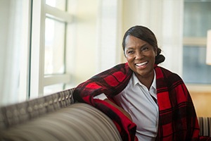 A middle-aged woman wearing a plaid shawl and smiling after receiving information about dental implant care in Carrollton