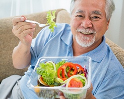 An older man sitting on a couch and eating a salad