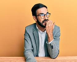 A younger man wearing a suit blazer and biting his nails