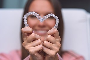 Woman holding Invisalign to camera in a heart shape