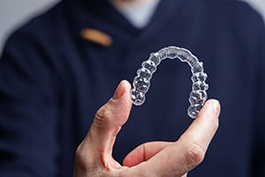 Man in navy scrubs holding Invisalign to camera