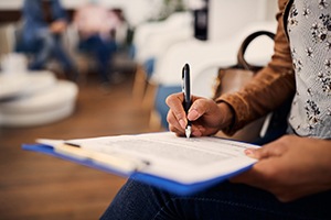 Hands filling out paperwork on blue clipboard in waiting room