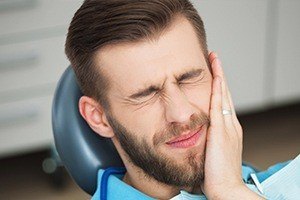 Man in dental chair holding cheek