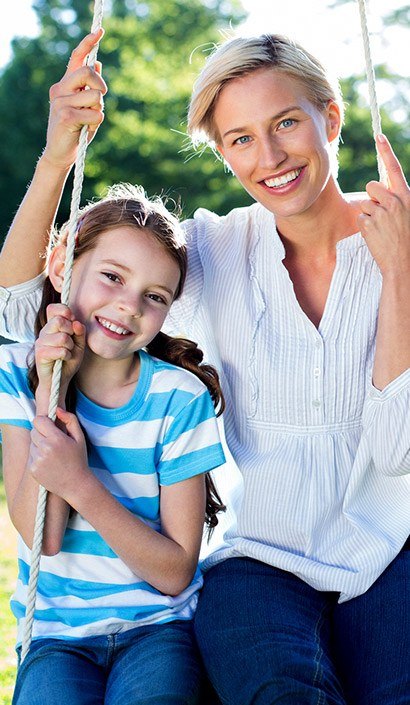 Smiling mother and daughter on swing outdoors