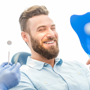 Man smiling in mirror in dentist’s chair