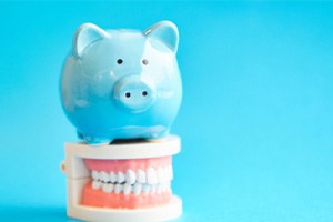 A blue piggy bank sitting on top of a white tooth model  