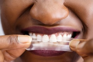 A close-up of a person using a teeth whitening strip 