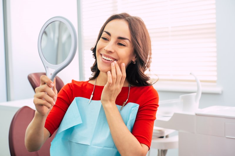 a woman looking at her smile in the mirror at the dentist office