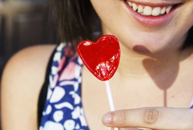 a young girl eating a hard sucker in the shape of a heart