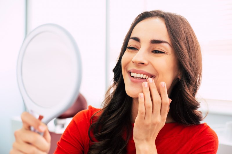 a young woman wearing a red blouse and admiring her new smile in the mirror