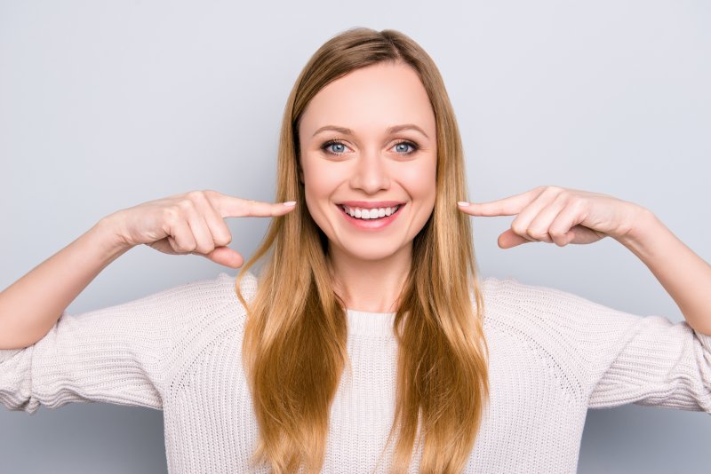 a young woman smiling and pointing to her brighter, whiter teeth