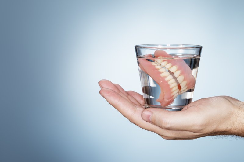 a person holding a glass of water that contains a full set of dentures