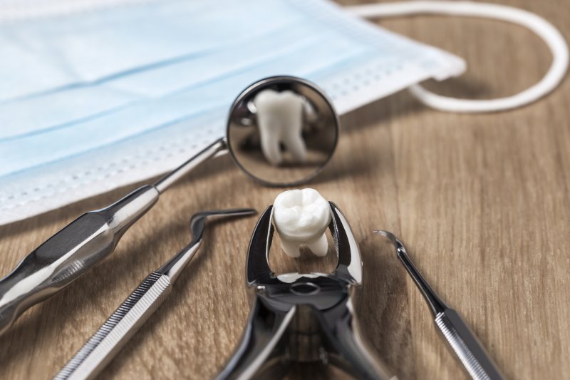 an extracted tooth and various dental instruments lying on a table next to a face mask