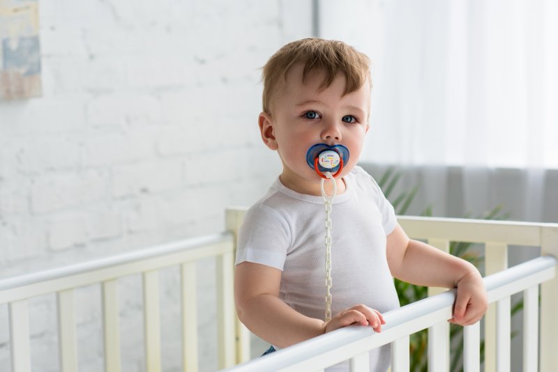 Toddler in a crib sucking on a pacifier