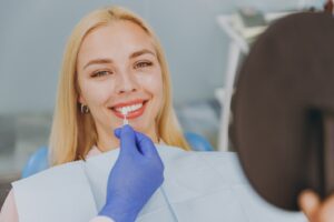 Gloved hand of dentist holding veneer up to patient’s smile.